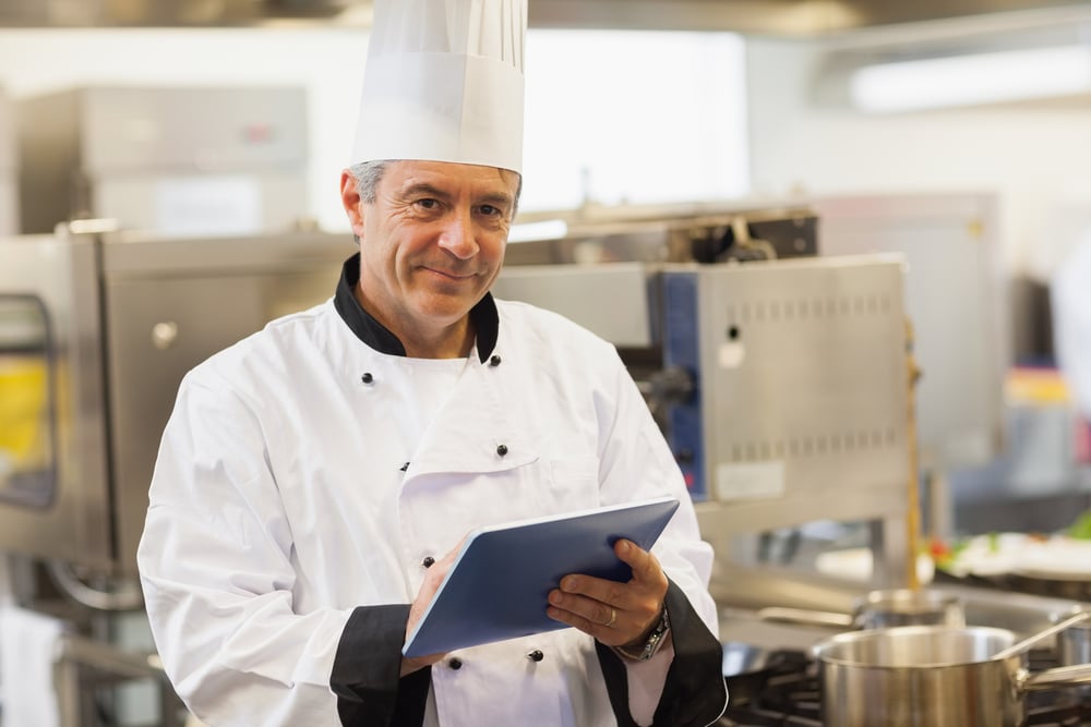 Chef using his digital tablet and looking at camera in the kitchen Chef using his digital tablet and looking at camera in the kitchen